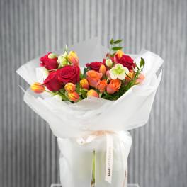 Bouquet of red and orange roses with tulips in a clear vase