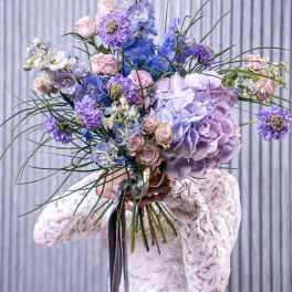 Bride holding a large pastel bouquet of hydrangeas, roses, and blue flowers