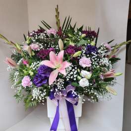 Pink lilies and mixed purple flowers in a white vase with ribbon