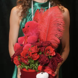 Red rose arrangement with a teddy bear and feathers in a round box