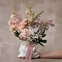 Handheld bouquet of pale pink flowers wrapped in white paper