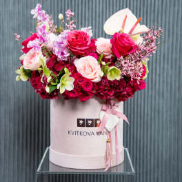 Pink and red floral arrangement in a round hat box with ribbon