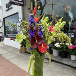 Tall tropical arrangement in a glass vase with red anthuriums and purple flowers
