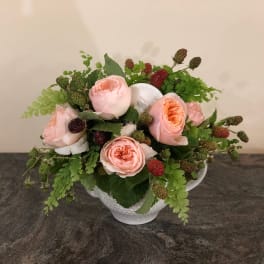 Pink roses arranged in a white teacup vase with green berries and foliage