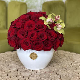 Red rose arrangement in a white vase with small orchid accents