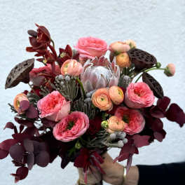 Handheld bouquet of pink and burgundy flowers with dark foliage