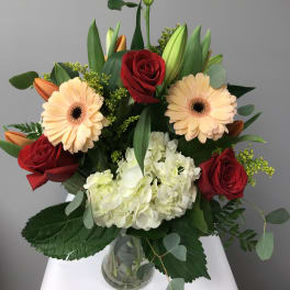 Bouquet of red roses, peach gerbera daisies, white hydrangea, and lilies in a glass vase