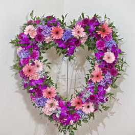 Heart-shaped floral wreath on a metal stand with pink, purple, and lavender blooms
