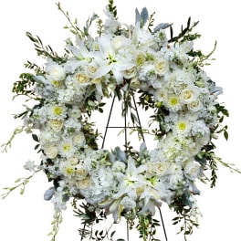 White floral wreath on a stand with roses and lilies