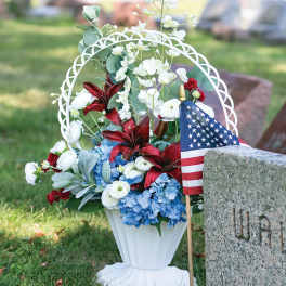 Memorial flower arrangement in a white urn with red, white, and blue flowers