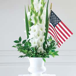 White gladiolus arrangement in a white urn with an American flag