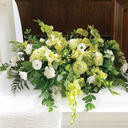 Green and white casket spray with roses, hydrangea, and other flowers on a white casket