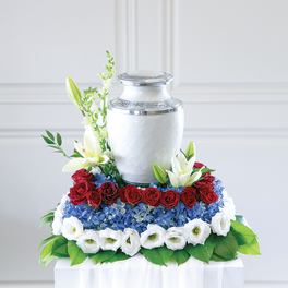 Floral urn arrangement with red roses, blue hydrangeas, and white lilies