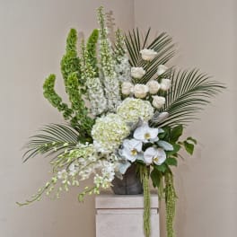 Tall white floral arrangement with orchids, roses, and palm fronds in a gray vase