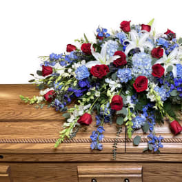 Casket spray with red roses, white lilies, and blue flowers