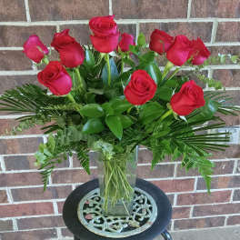 Red roses arranged in a clear glass vase with mixed greenery