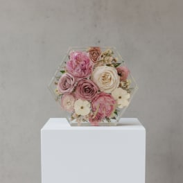 Hexagonal floral display with pink and cream roses in a clear frame
