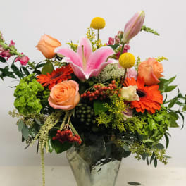 Mixed bouquet with pink lily, orange roses, and gerbera daisies in a glass vase