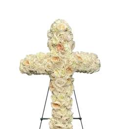 Cross-shaped floral tribute made of cream and blush roses on an easel