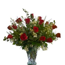 Tall arrangement of red roses with small white blooms in a clear glass vase