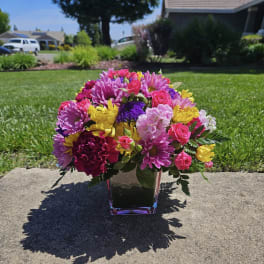 Bright mixed bouquet in a square glass vase on a sidewalk