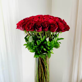 Tall vase of red roses with green foliage on a small table