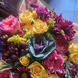 Hand-tied bouquet of yellow roses, pink blooms, purple mums, and ornamental cabbage in plaid wrap