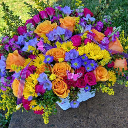 Colorful bouquet of roses, daisies, and purple blooms in a white basket