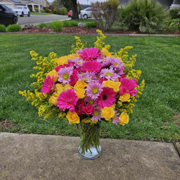 Bright mixed bouquet of pink, yellow, and lavender flowers in a glass vase