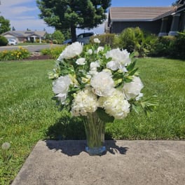 White floral arrangement in a clear glass vase on a sidewalk