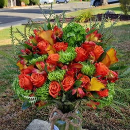 Bouquet of orange roses, calla lilies, and mixed blooms in a glass vase