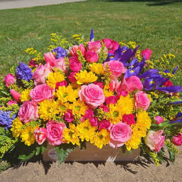 Bright mixed bouquet of pink roses, yellow daisies, and purple irises in a wooden box