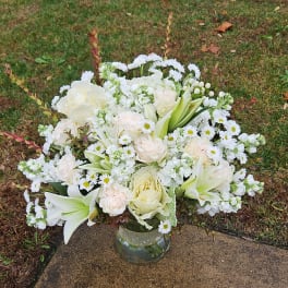 White floral arrangement in a clear glass vase on a sidewalk