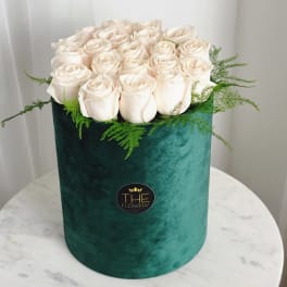 White roses arranged in a green velvet hat box with fern accents