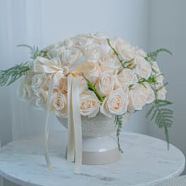Cream rose bouquet in a white pedestal vase with a satin ribbon