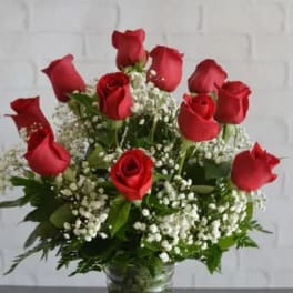 Red roses arranged in a clear glass vase with white baby's breath