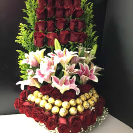 Tall arrangement of red roses, lilies, and gold-wrapped chocolates