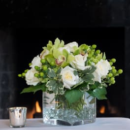 White roses and green orchids arranged in a glass vase with decorative beads.