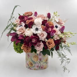 Mixed bouquet of roses, orchids, and tulips in a floral-patterned box