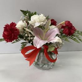Pink lily and red-white carnations in a glass vase with a red ribbon