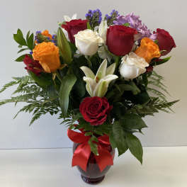 Bouquet of red, white, and orange roses in a glass vase with a red ribbon