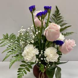 Pink roses and white carnations in a small vase with purple filler flowers