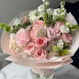 Pink and white bouquet of roses and mixed blooms wrapped in pale paper