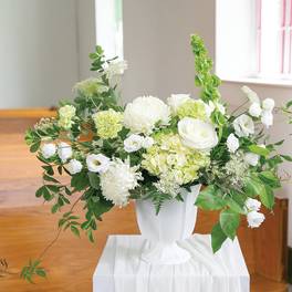 White floral arrangement in a white vase with green accents