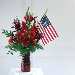 Red floral arrangement in a glass vase with an American flag