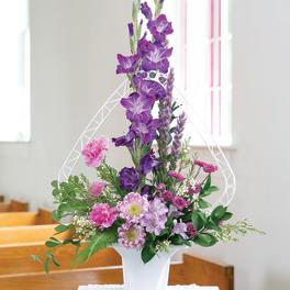 Purple and pink floral arrangement in a white vase with a decorative arch
