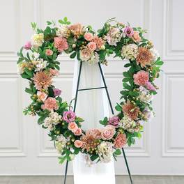 Heart-shaped floral wreath on a stand with pink and white flowers