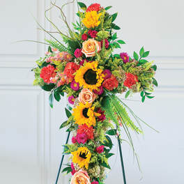 Tall floral cross on a stand with sunflowers, roses, and carnations