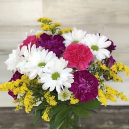 Bouquet of white daisies, pink carnations, and yellow filler in a glass vase