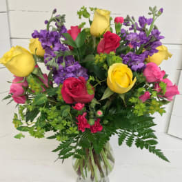 Bouquet of yellow, pink, red, and purple roses in a clear glass vase